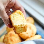 A biscuit that's been buttered being held in a hand.