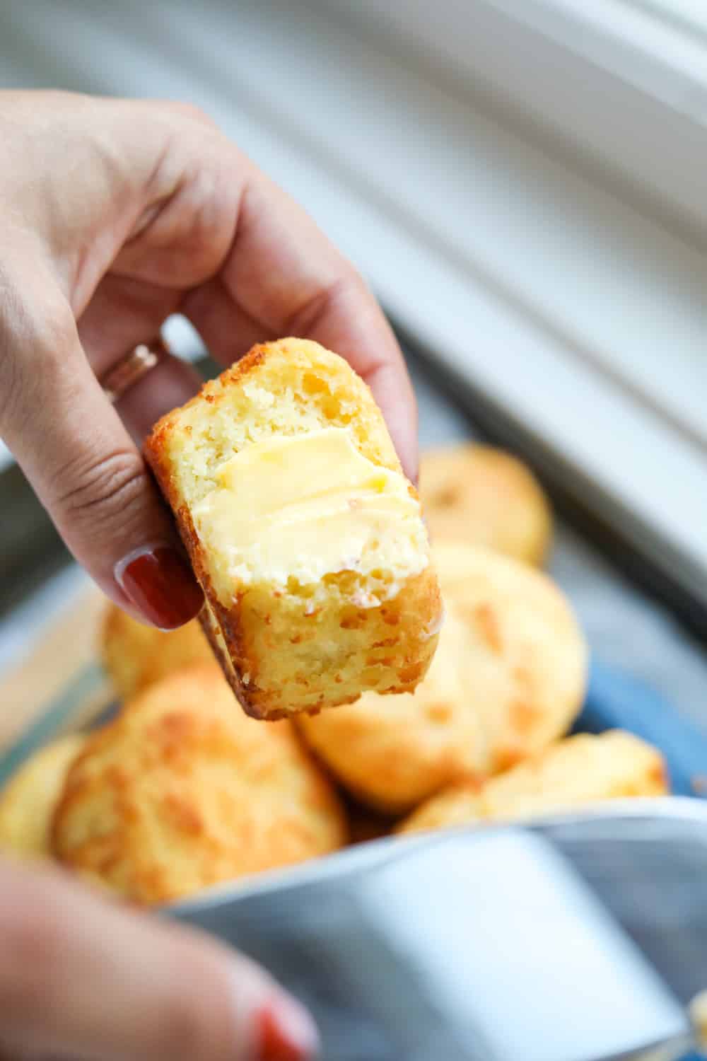 A biscuit that's been buttered being held in a hand.