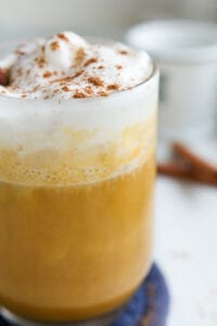 A pumpkin spice latte in a clear cup topped with whipped cream and spices.