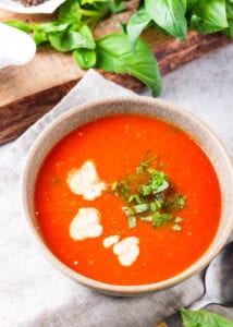 Tomato soup in a bowl that has heavy cream and chopped basil added to it.