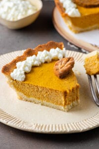 A slice of pumpkin pie with a piece take off of it.