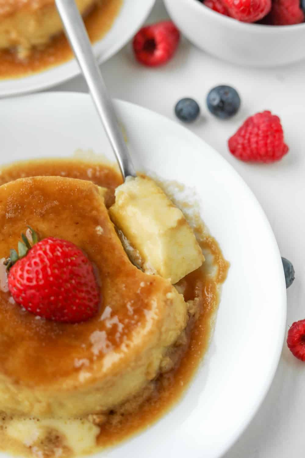 Flan on a white plate with a piece of the flan on a small spoon.