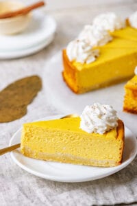 The side of a slice of pumpkin cheesecake on a white plate.