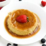 Flan on a white plate with a strawberry on top of it.