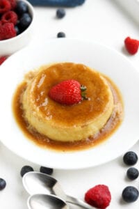 Flan on a white plate with a strawberry on top of it.