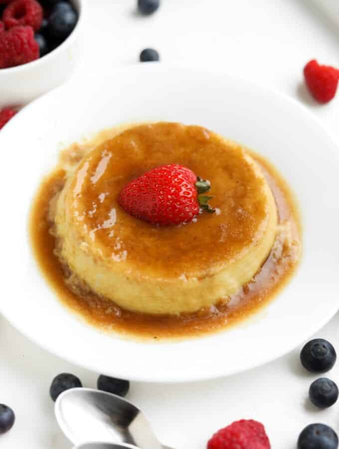 Flan on a white plate with a strawberry on top of it.