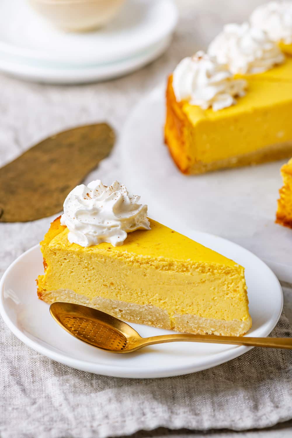 Cheesecake on a white plate with a gold spoon set next to it.