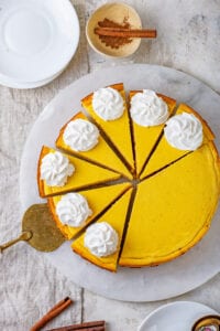 Pumpkin cheesecake cut into slices with a gold serving utensil under one of the slices.