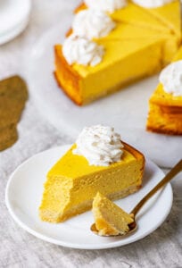 A slice of pumpkin cheesecake on a white plate with the rest of the slices behind it.