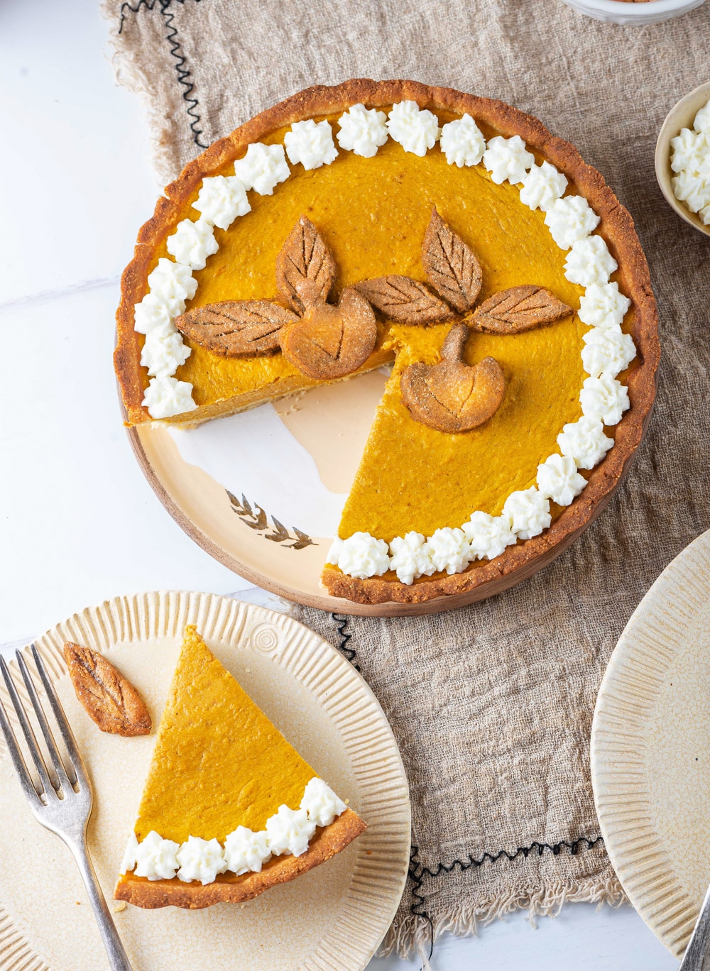 A slice of pumpkin pie on a plate set next to the entire pie.