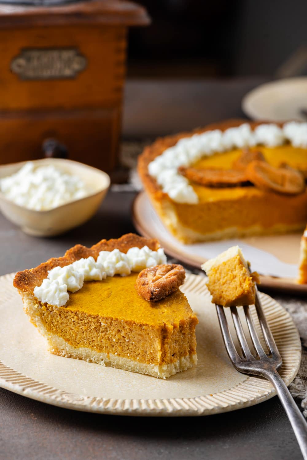 A slice of pumpkin pie on a plate with a fork holding a piece of the pie.