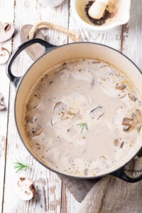 Mushroom soup in a black pot on a white wooden table.