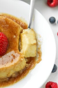 A small piece of flan on a spoon set on a white plate.