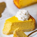 A slice of pumpkin cheesecake on a plate with a spoon holding a piece of it.