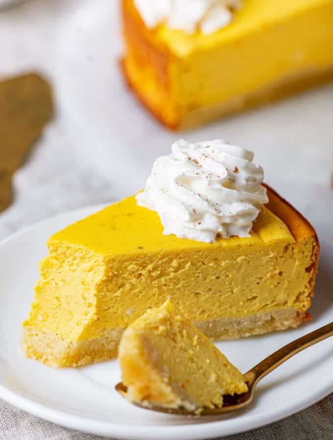 A slice of pumpkin cheesecake on a plate with a spoon holding a piece of it.