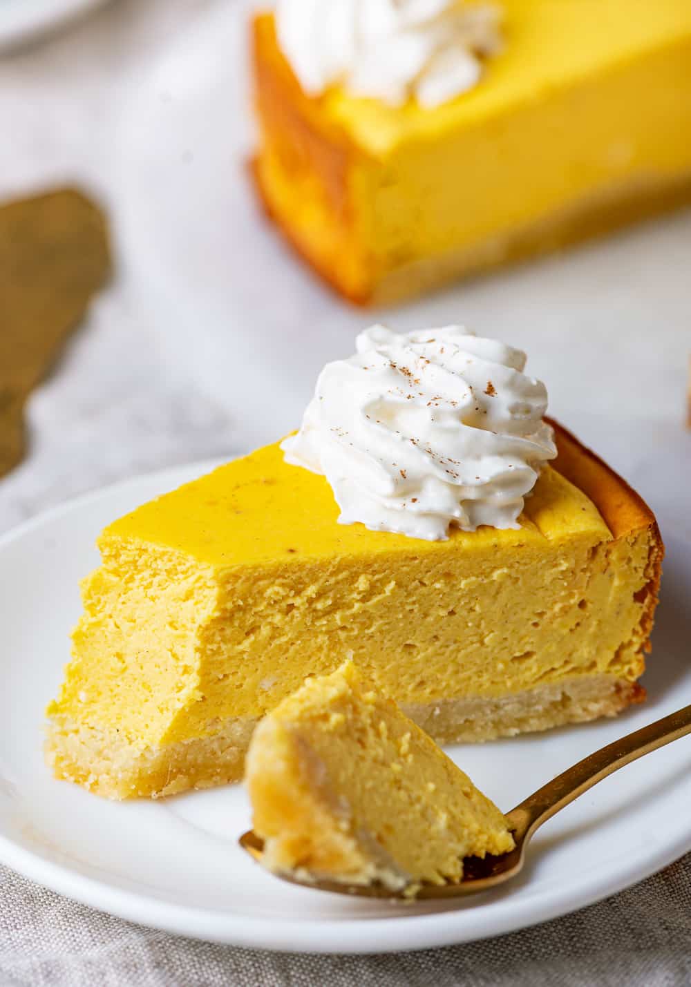 A slice of pumpkin cheesecake on a plate with a spoon holding a piece of it.