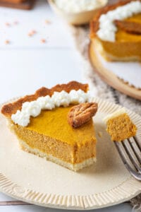 A plate with a slice of pumpkin pie, and a fork holding a piece of the pie next to it.