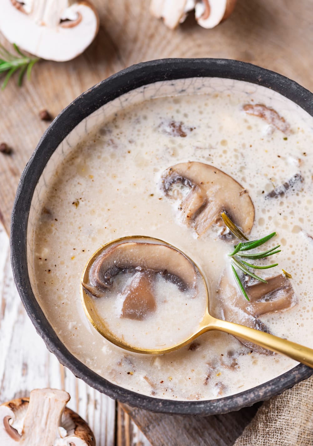 A golden spoon taking soup out of a black bowl.