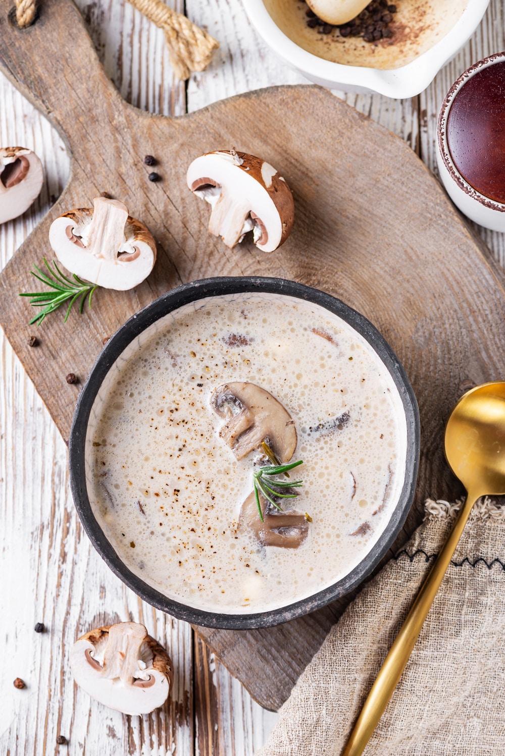 A white table with a bowl of creamy mushroom soup set on top of a cutting board.