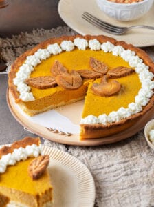 A pumpkin pie that's missing a piece set on a serving plate.