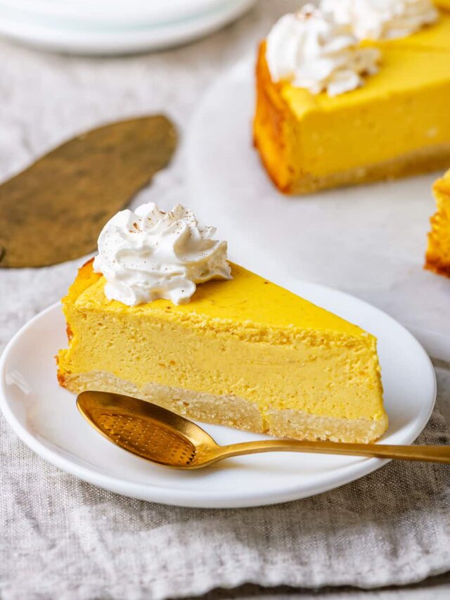 Cheesecake on a white plate with a gold spoon set next to it.