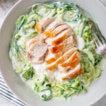 A white bowl filled with zucchini noodles, chicken, and alfredo sauce set on a blue stripped napkin.