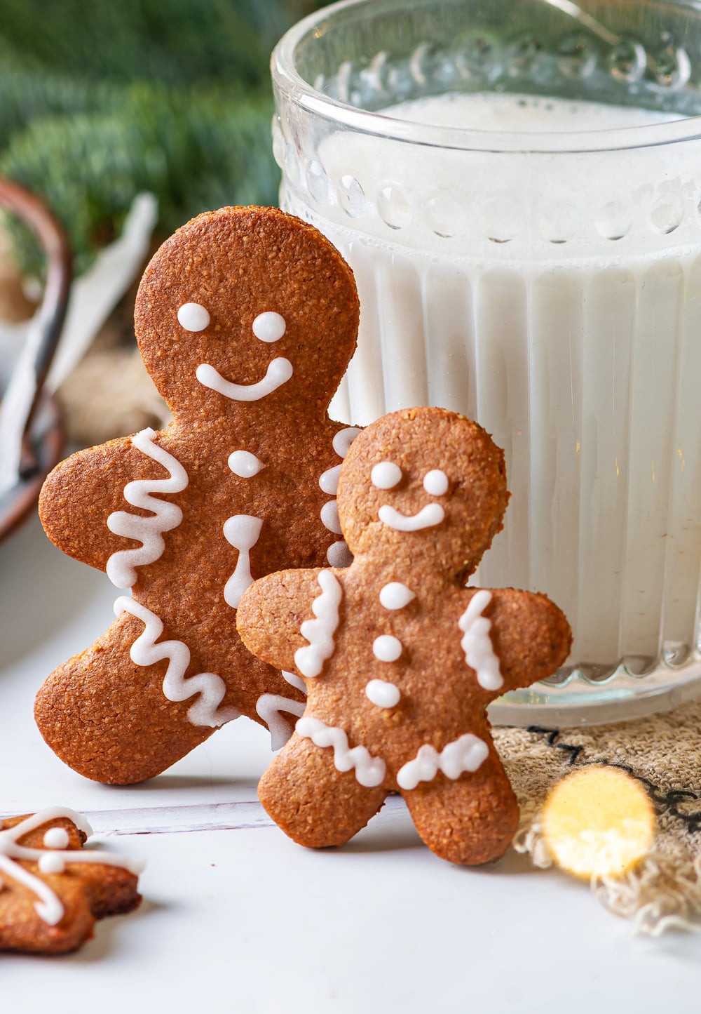 A large gingerbread man cookie and a small one leaning against a glass of milk.