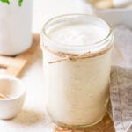 A mason jar filled with alfredo sauce, the jar is on a table.