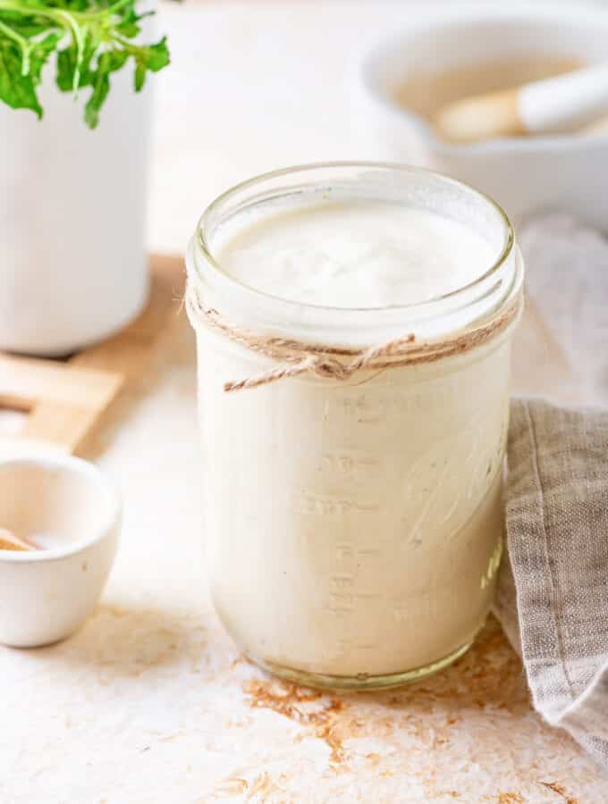 A mason jar filled with alfredo sauce, the jar is on a table.