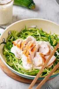 A bowl full of zucchini noodles, alfredo sauce, and cut up chicken.
