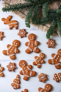 Gingerbread cookies on a white table. Green pine branches are above the cookies.
