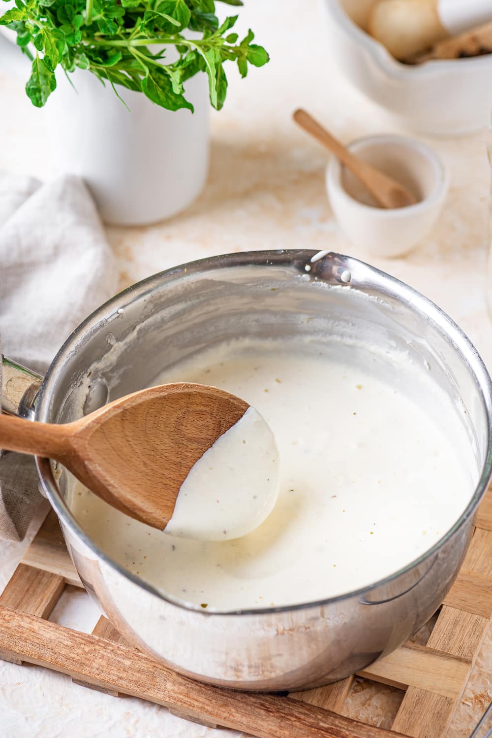 Alfredo sauce in a pot with a wooden spoon coated in sauce above it.