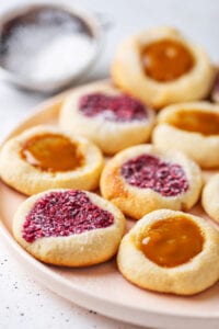Cookies filled with peach jam and raspberry jam on a nude colored plate.