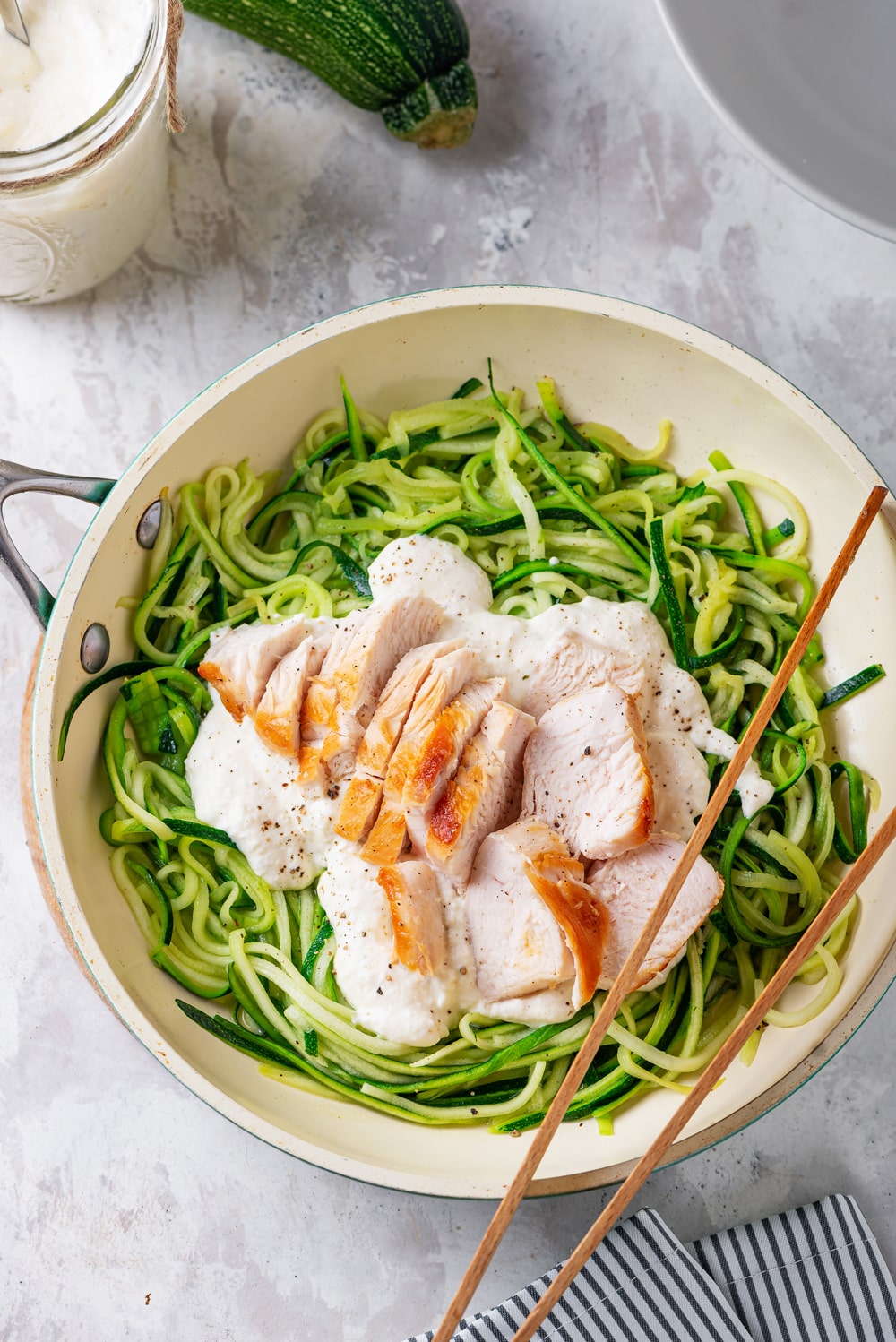 A pot full of cooked zucchini noodles that have been topped with alfredo sauce and cut up chicken.