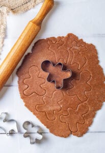 A rolling pin above dough that has been rolled out, and a cookie cutter on top of the dough.