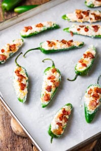 A baking sheet of uncooked jalapenos that have been stuffed with cream cheese and bacon.
