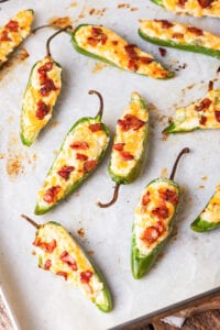 Jalapeno poppers topped with bacon on a baking sheet lined with parchment paper