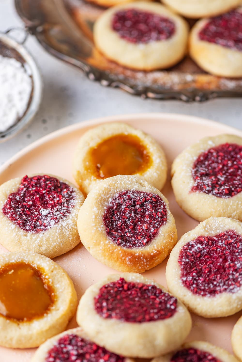 Thumbprint cookies on a nude plate. There are more cookies on a silver plate behind them.