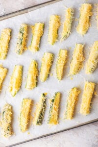 Slices of uncooked zucchini coated in breading laying on a baking sheet.