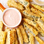 Breaded zucchini slices next to a cup of dipping sauce.