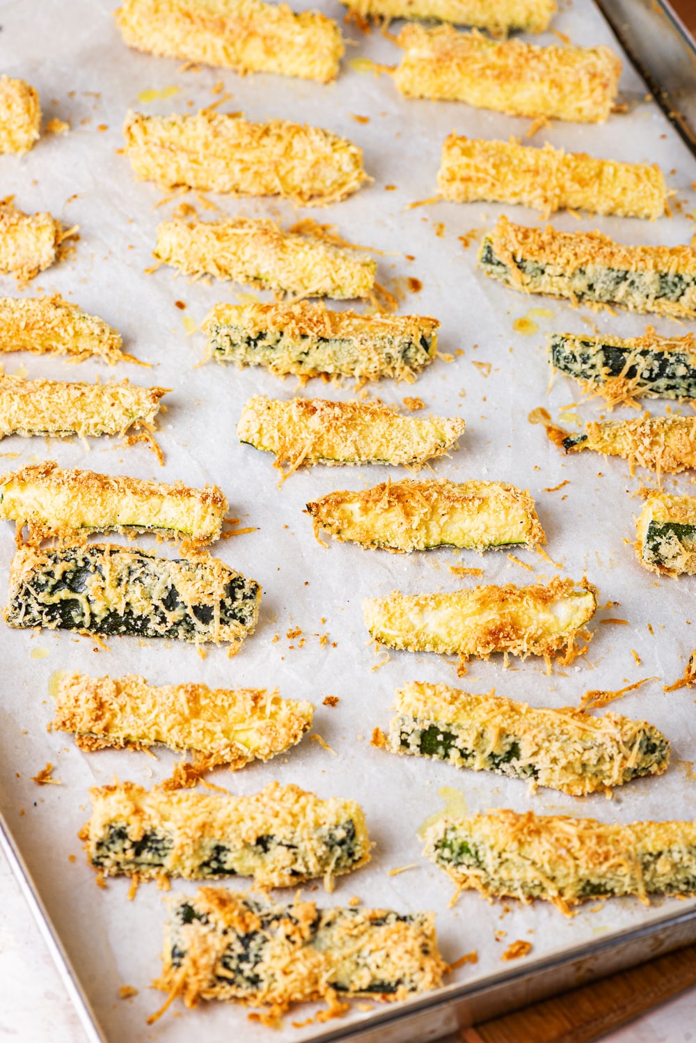 Slices of breaded and cooked zucchini on a baking sheet lined with parchment paper.