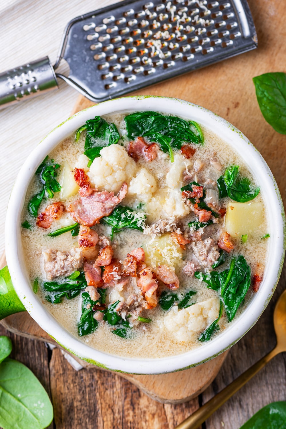 A bowl filled with zuppa toscana soup. The soup has sausage, greens, cauliflower, and kohlrabi in it. It's also topped with bacon.