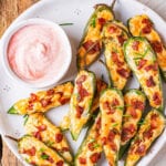 Jalapeno poppers piled on a white plate next to a pink dipping sauce.