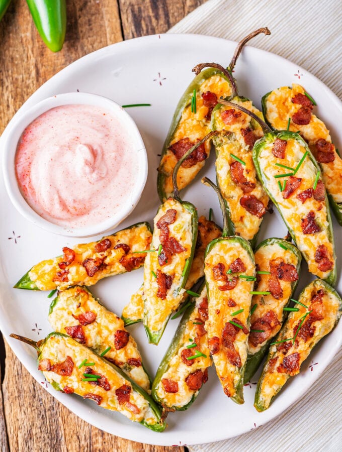 Jalapeno poppers piled on a white plate next to a pink dipping sauce.