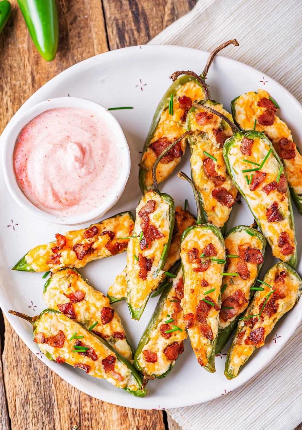 Jalapeno poppers piled on a white plate next to a pink dipping sauce.