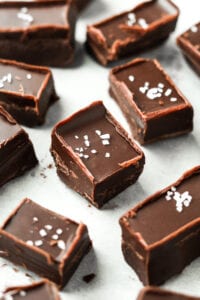 Chocolate fudge topped with coarse salt on a white piece of paper.