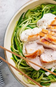 A white pot filled with zucchini noodles with alfredo sauce and chicken.