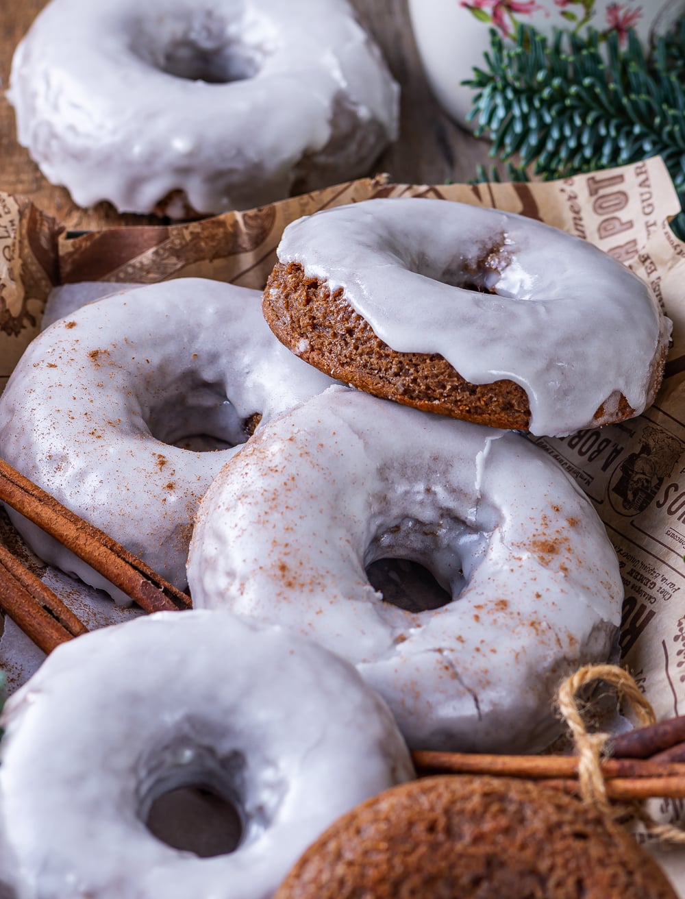 A close up of four glazed gingerbread donuts overlapping each other on a piece of paper. One glazed gingerbread donut is behind the piece of paper.