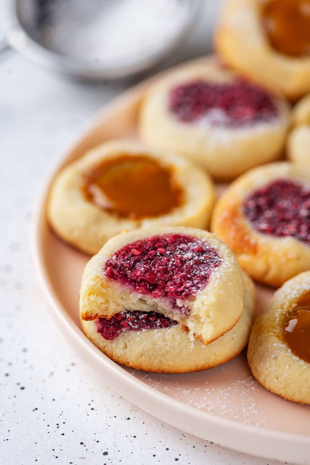 A thumbprint cookie with a bite taken out of it, stacked on top of another cookie. There are more cookies behind them.