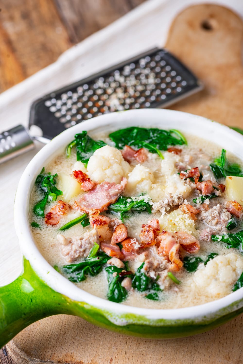 A green bowl filled with zuppa toscana soup. The bowl is set on a wooden cutting board.